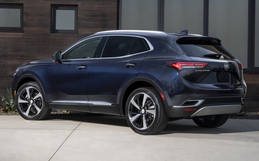Dark blue Buick Envision SUV parked on a concrete driveway in front of a modern wood-paneled building with windows.