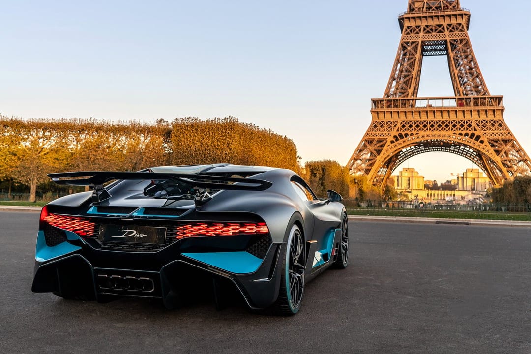 Bugatti Divo supercar in matte grey with blue accents parked near the Eiffel Tower in Paris at sunset.