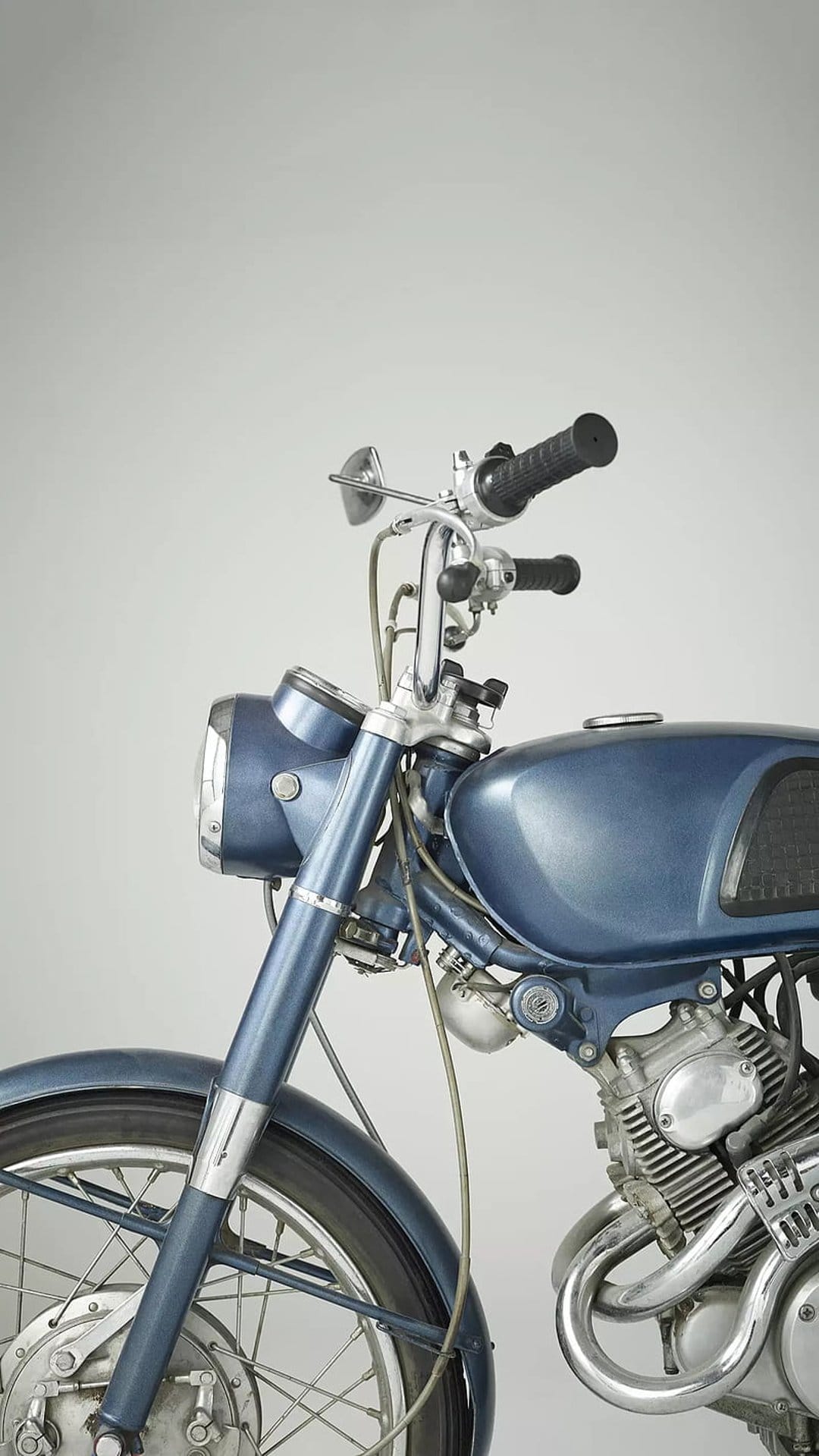 Blue vintage motorcycle front assembly with a chrome headlight and spoked wheels against a soft background.
