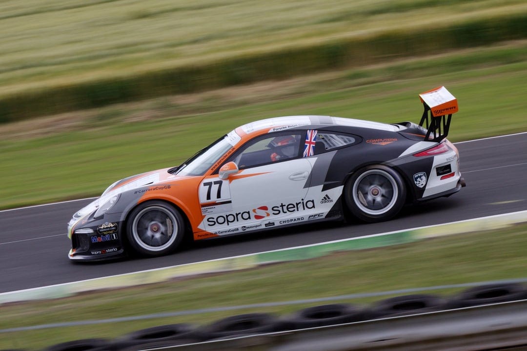 Porsche 911 GT3 Cup race car with number 77 rounds a track corner showing motion blur and orange accents.