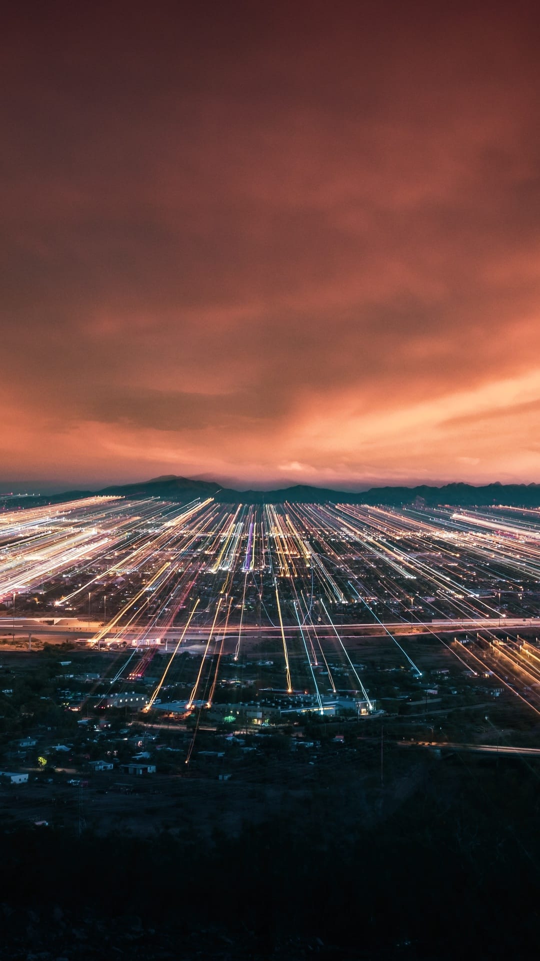 Glowing orange light trails zoom outward from a central city point under a dark red and orange twilight sky.