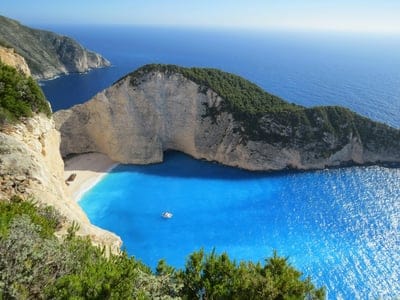 Navagio Beach shipwreck rests on white sand surrounded by sheer limestone cliffs and bright turquoise ocean water.