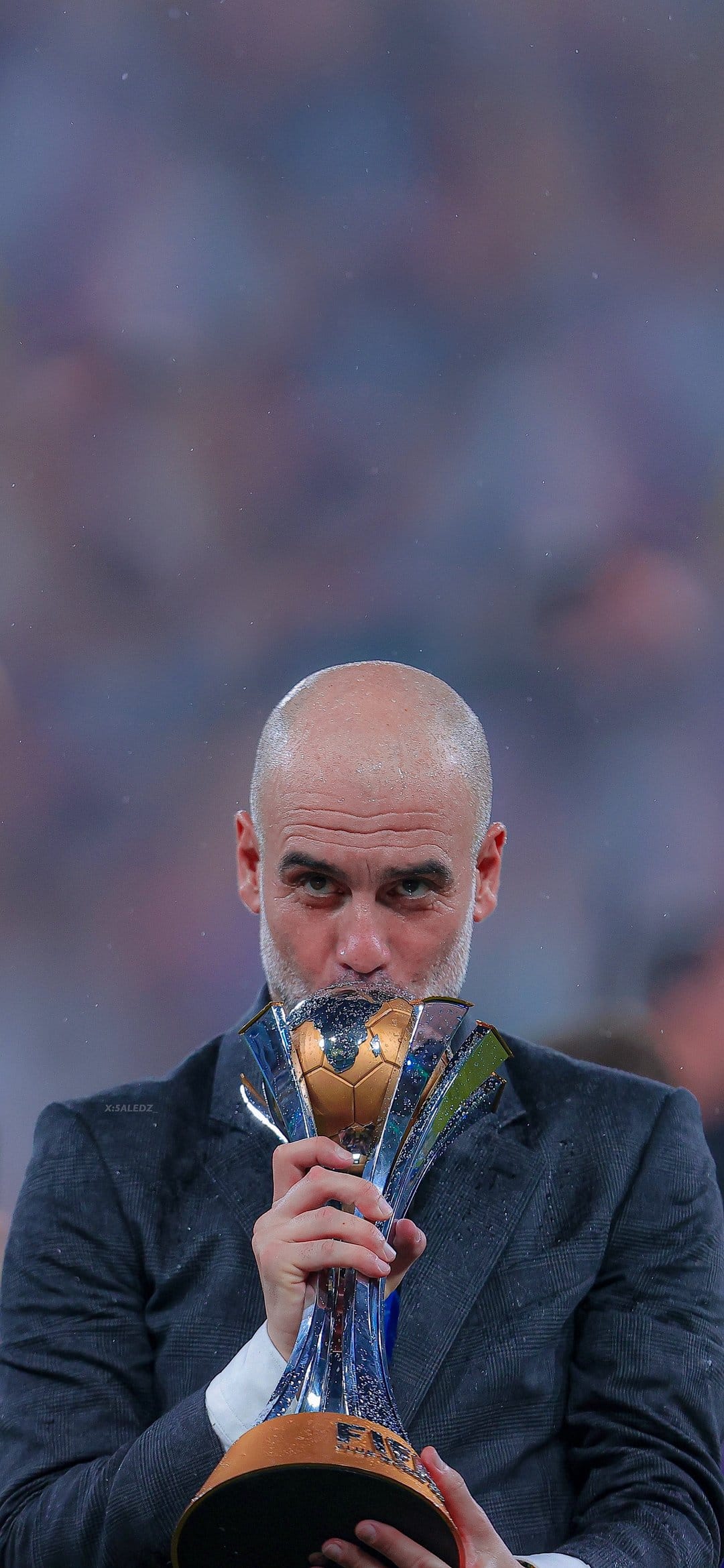 Pep Guardiola kisses the golden FIFA Club World Cup trophy while wearing a dark Manchester City team sweater.