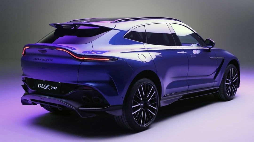Rear three-quarter view of a metallic purple Aston Martin DBX 707 SUV with signature LED taillights in a studio.