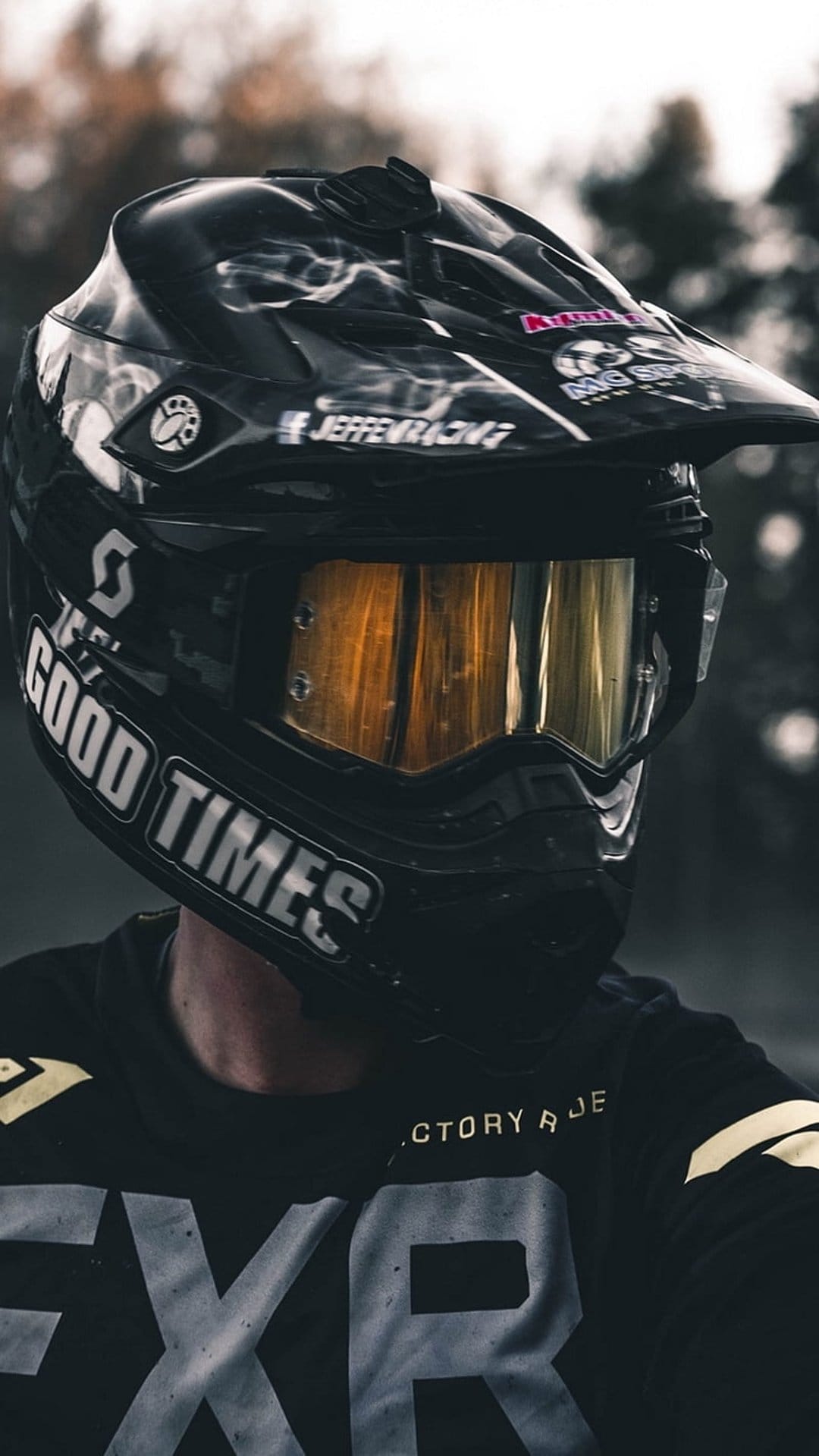 Motocross rider wearing a black helmet with gold goggles and a jersey featuring bold white lettering.