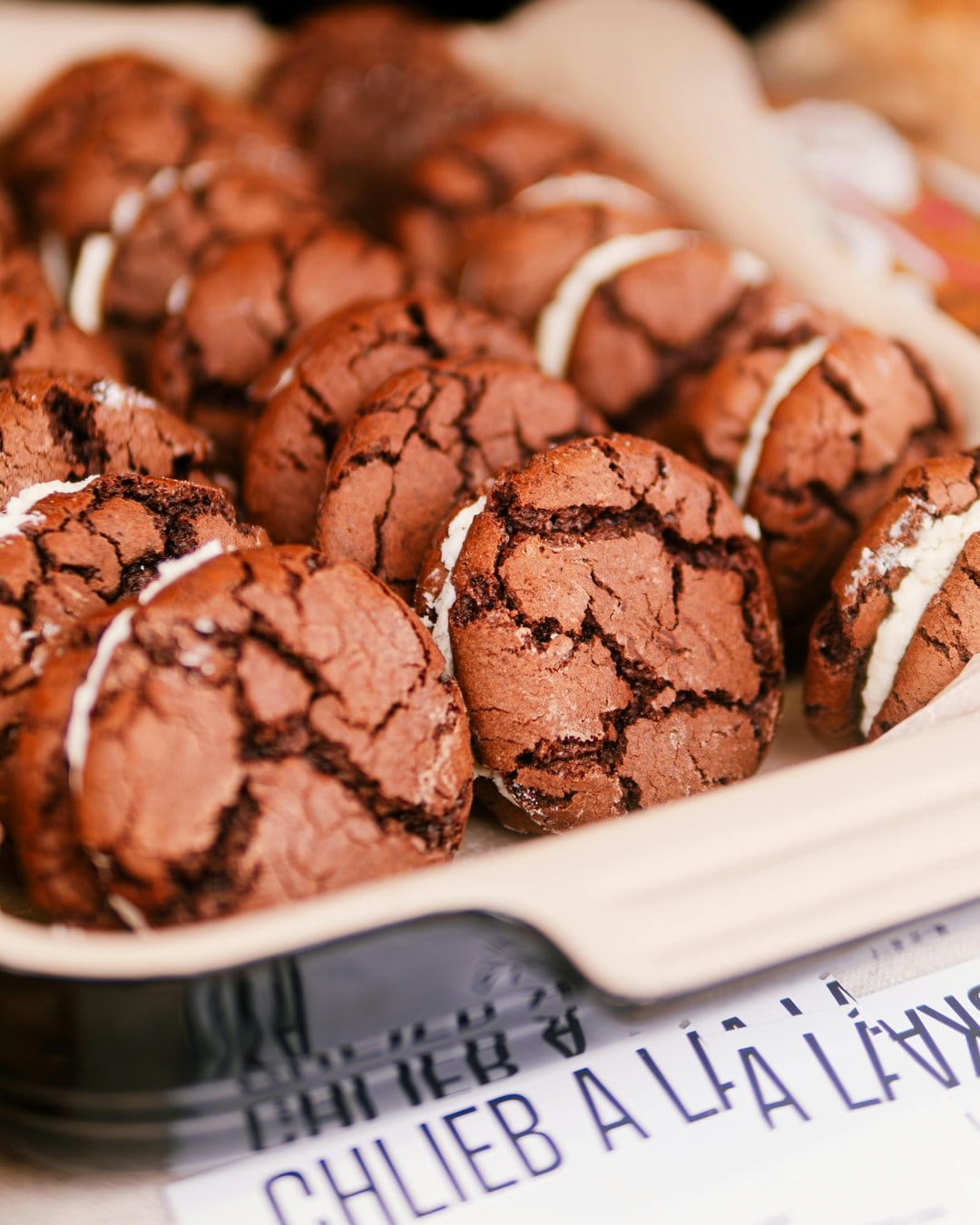 Chocolate crinkle sandwich cookies dusted with sugar and filled with cream in a sharp macro vertical view.