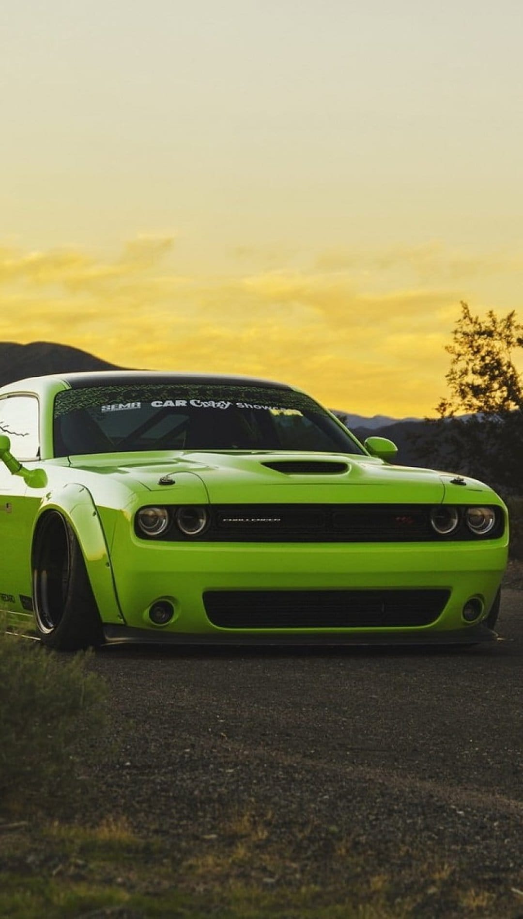 Lime green Dodge Challenger Hellcat with a widebody kit parked against a vibrant orange and yellow mountain sunset.