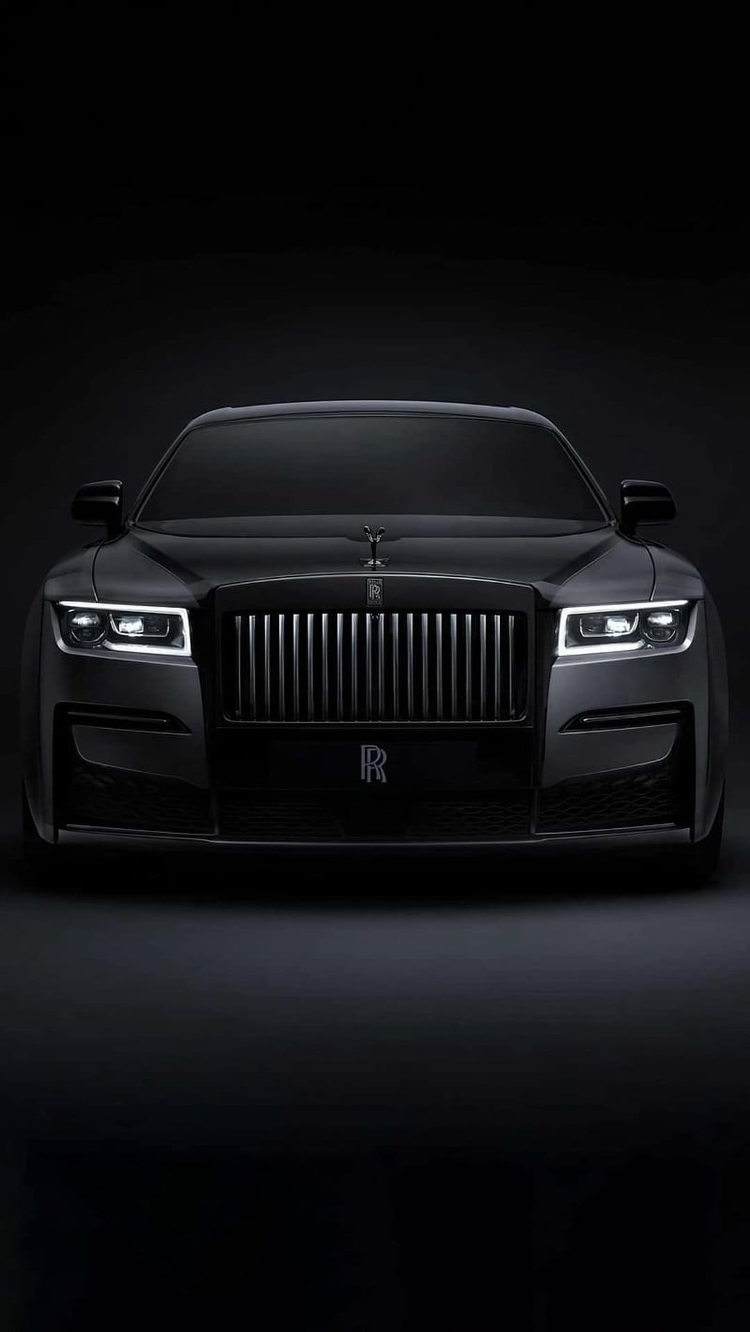 Black Rolls-Royce Ghost front grille with illuminated headlights and Spirit of Ecstasy mascot on the hood.