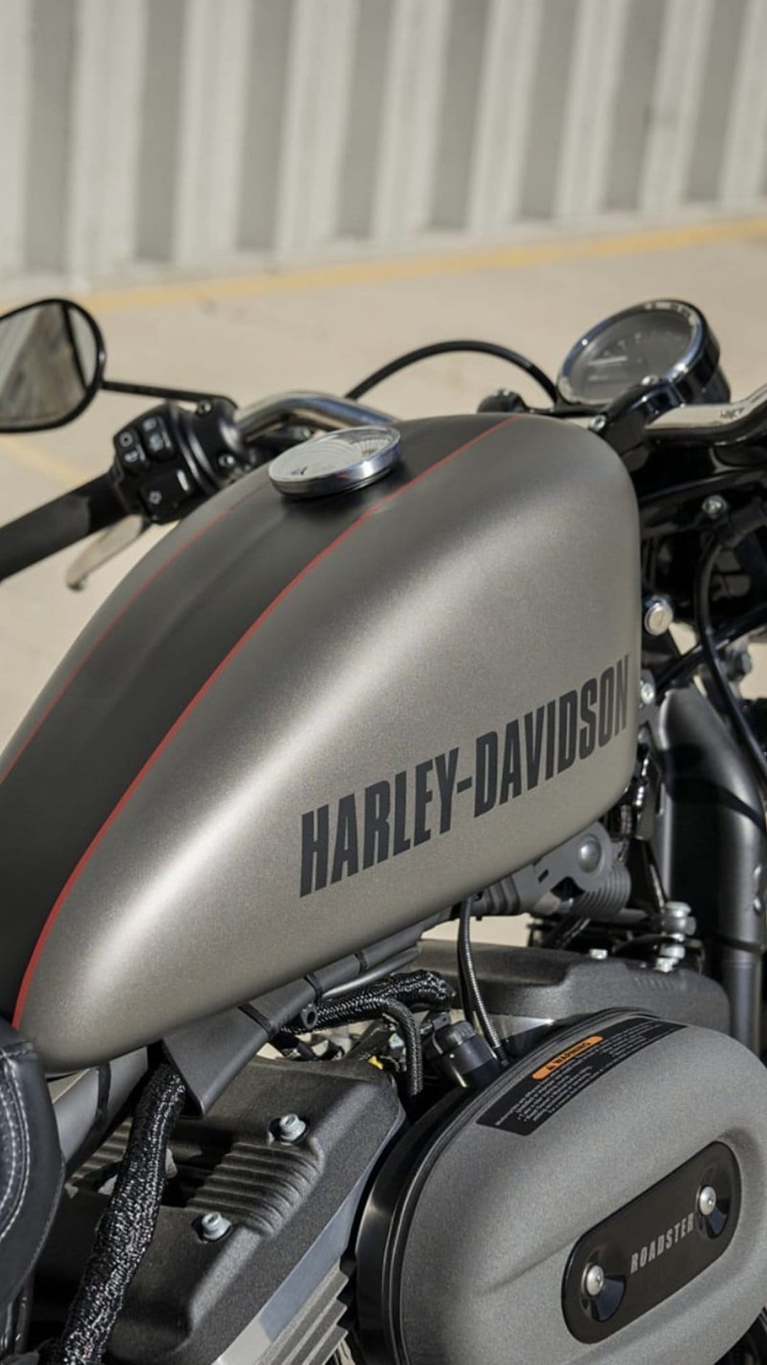 Harley-Davidson fuel tank featuring matte gray finish, red racing stripes, and polished chrome engine details.