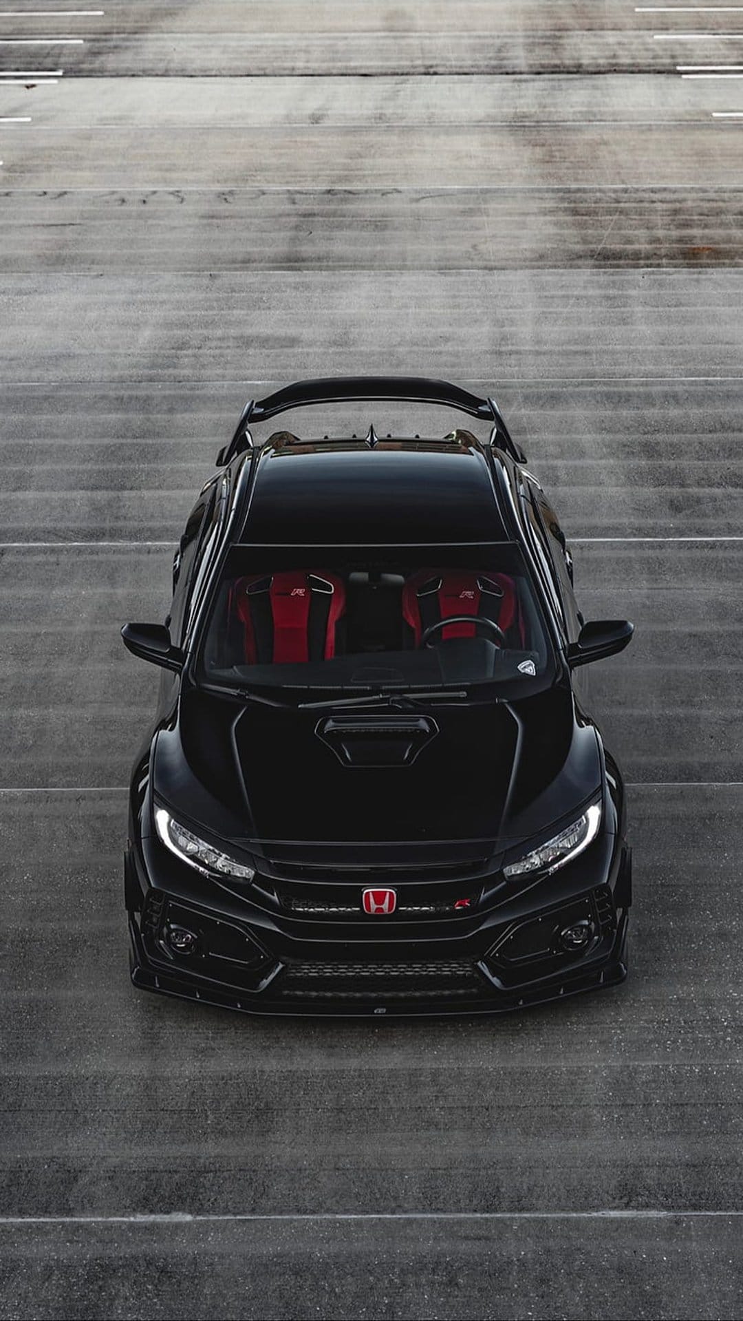 Black Honda Civic Type R with a rear spoiler and red seats parked on a gray asphalt track with white lines.