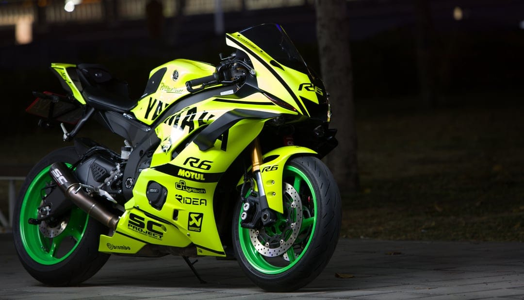 Neon yellow Yamaha R6 motorcycle with black graphics and green rim accents parked in a dark night environment.