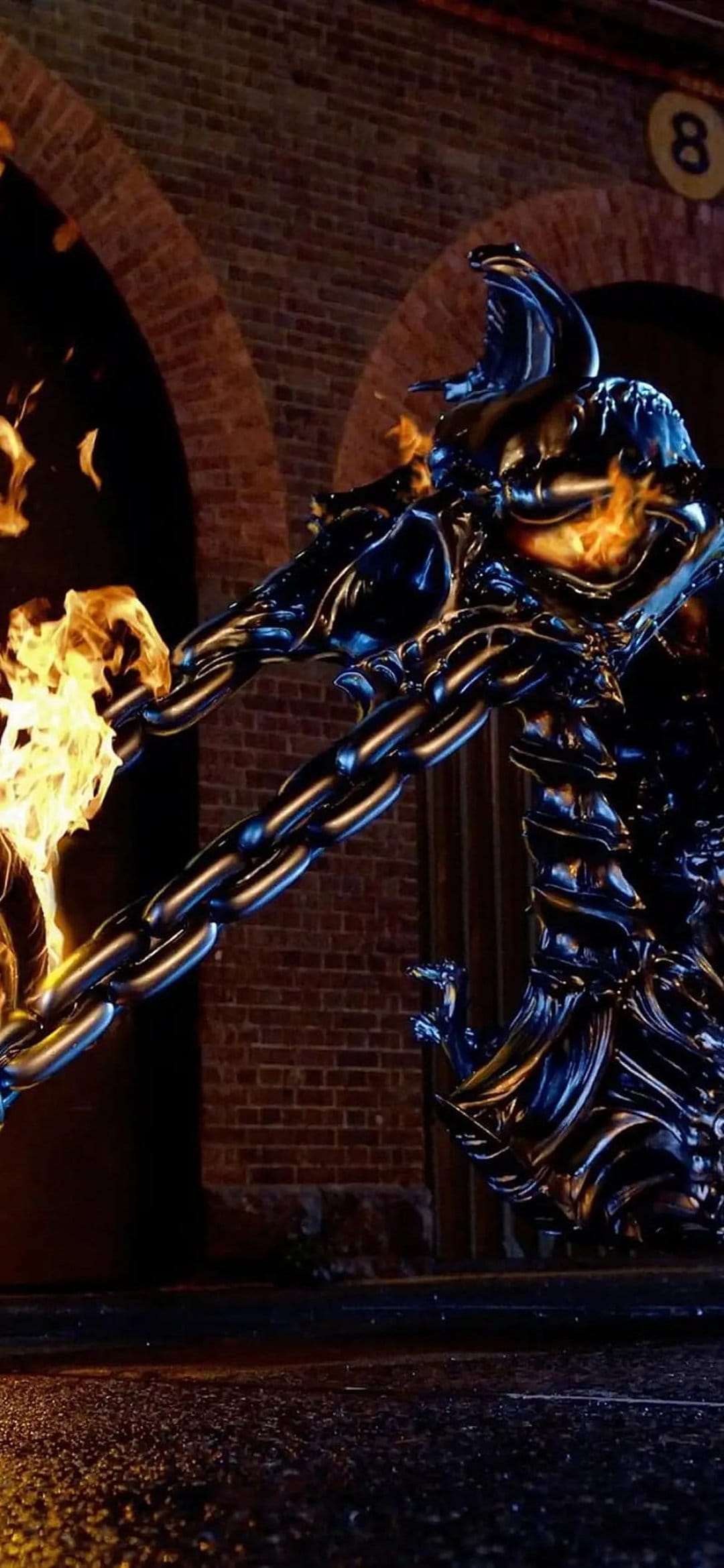 Ghost Rider wielding a glowing fire chain in front of a stone archway with wet ground reflections.
