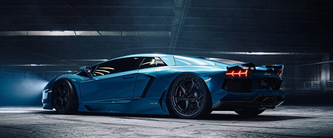 Blue Lamborghini Aventador in a dark garage with glowing red taillights and carbon fiber wheels in landscape view.