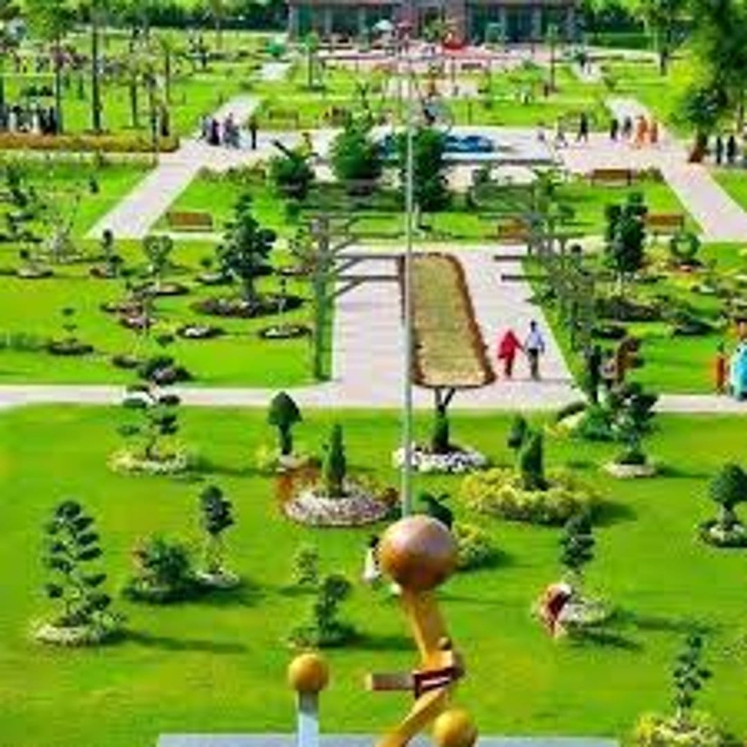 Manicured green lawns and geometric garden paths seen from above with small figures walking in a sunny park.