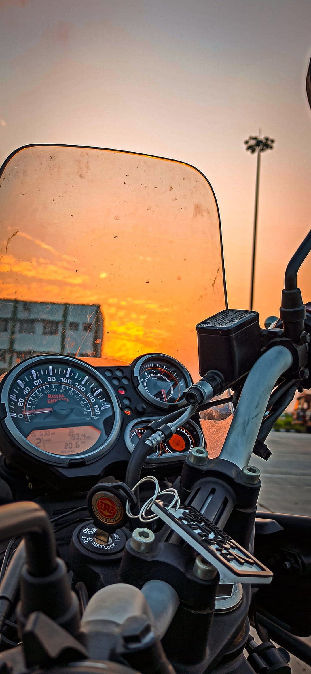 Royal Enfield Himalayan motorcycle dashboard with sunset reflections on the windshield and glowing gauges.