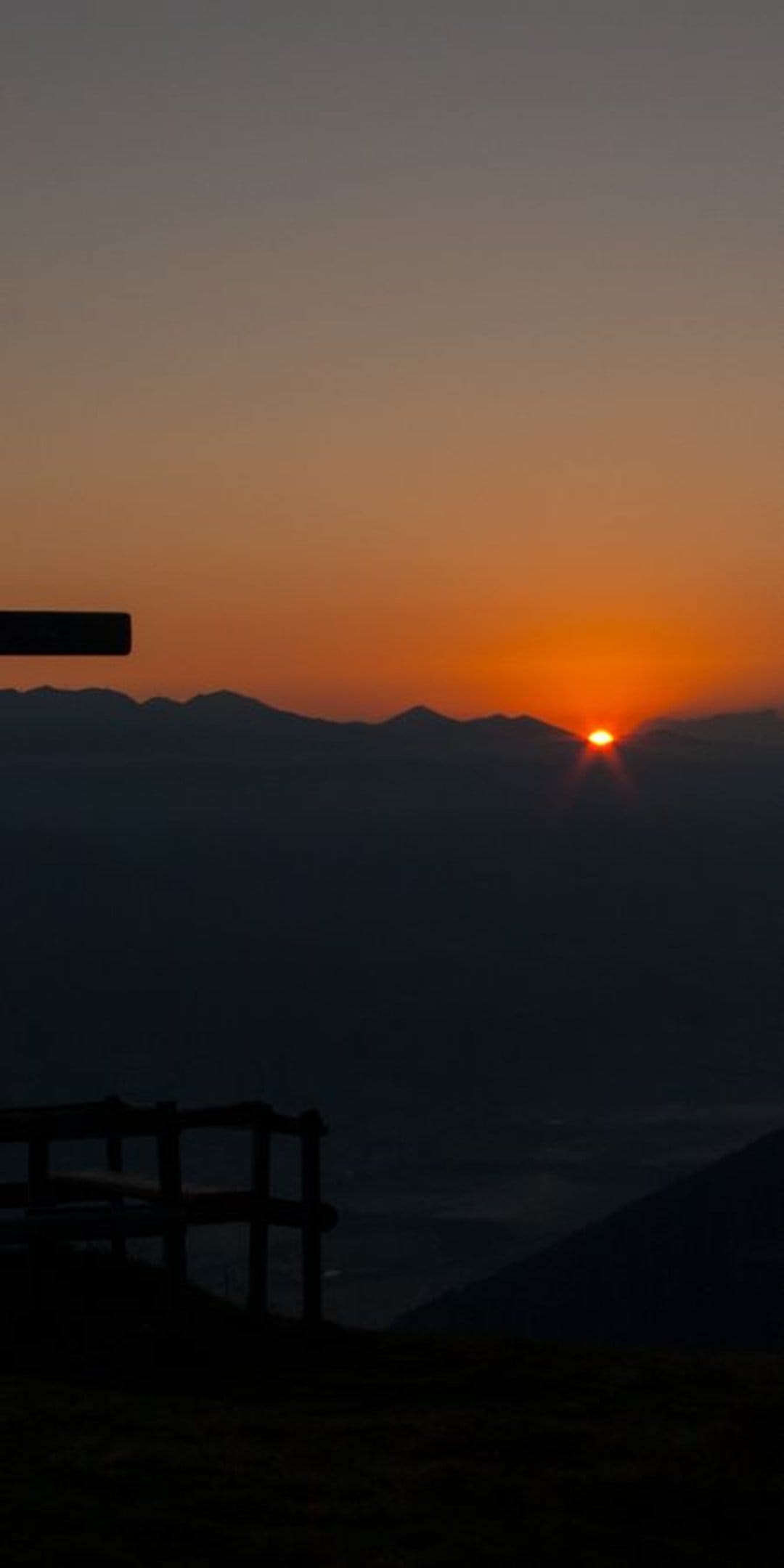 Silhouetted mountain peaks rise above a cloud-filled valley as a bright orange sun emerges during a vivid dawn.