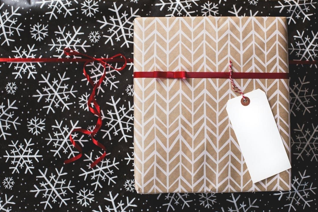 Brown chevron gift box tied with a red ribbon and white tag centered on a black snowflake-patterned background.