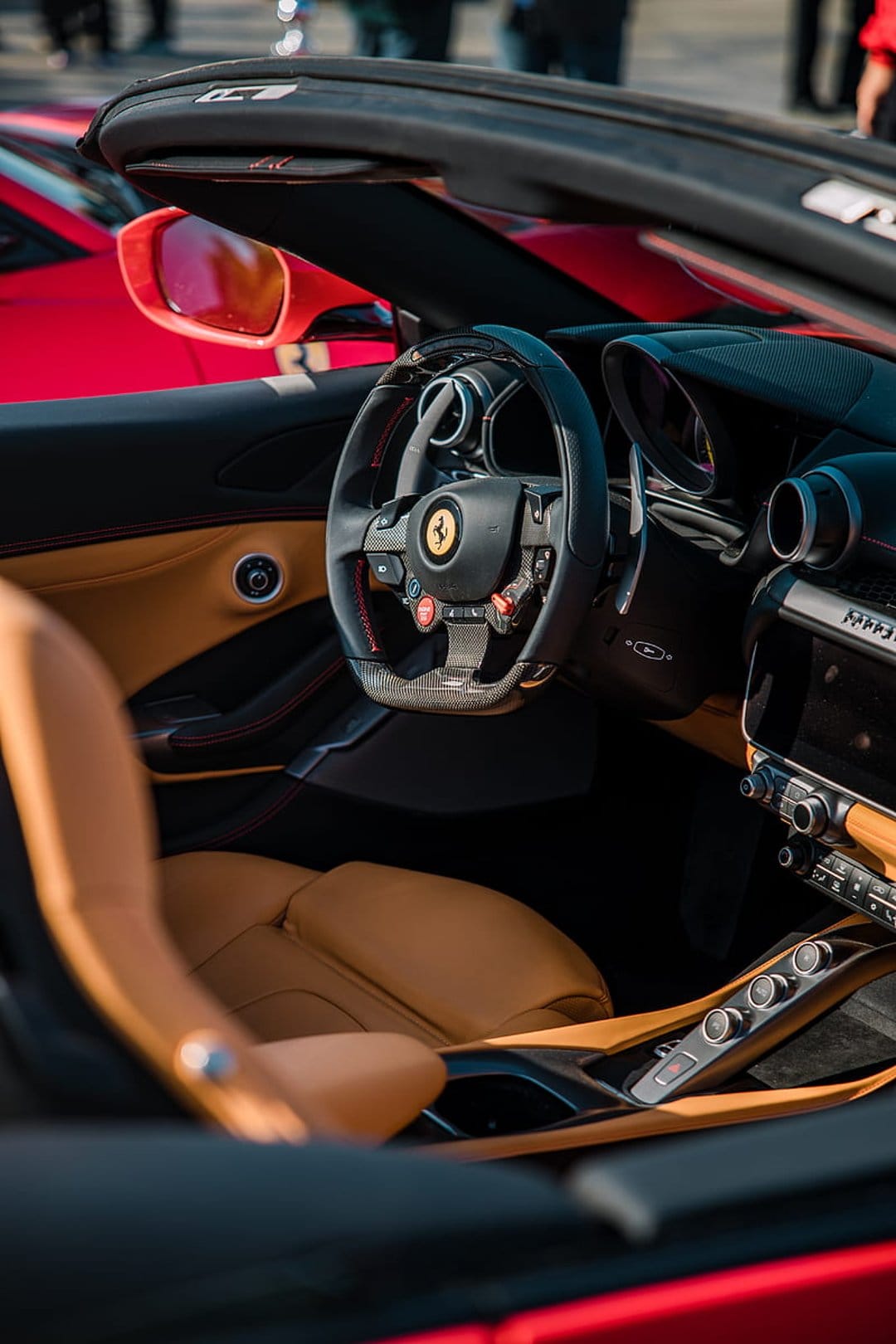 Ferrari steering wheel with a prancing horse emblem near tan leather seats and a carbon fiber dashboard.