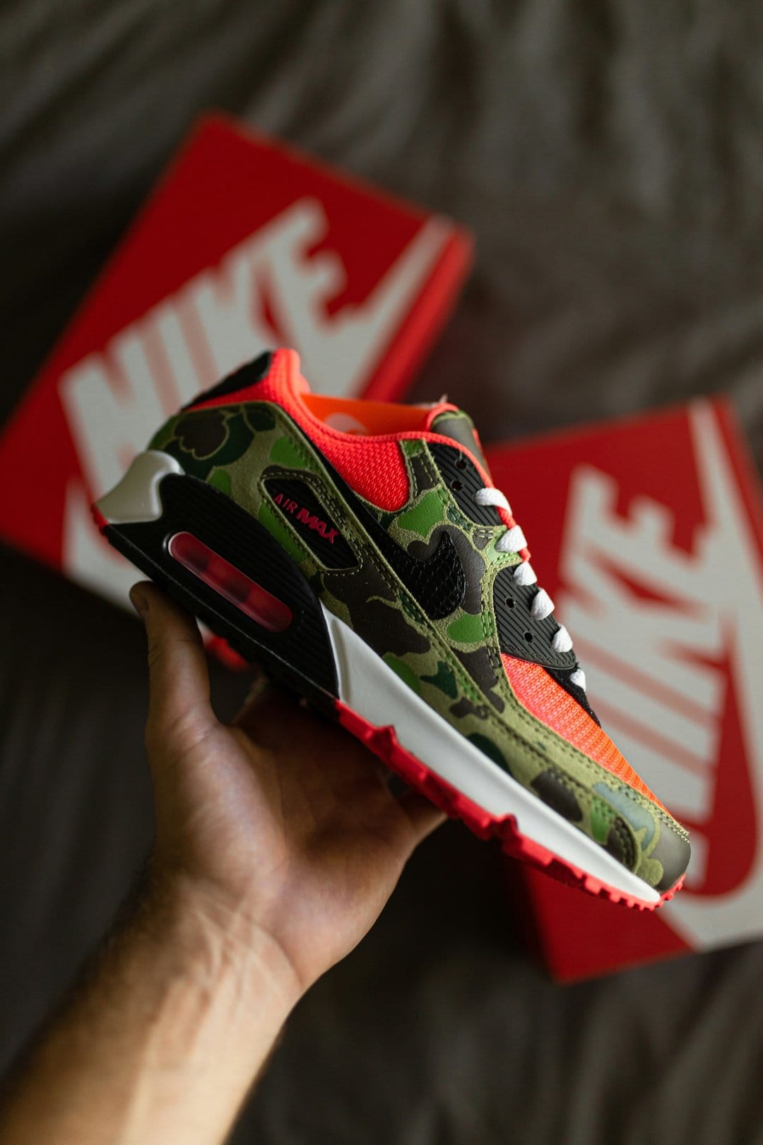 Nike Air Max 90 sneaker featuring woodland camouflage patterns and bright orange mesh on the toe box area.