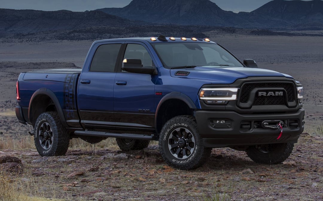 Blue Ram 2500 Power Wagon truck on rocky ground with mountains and twilight sky in the background.