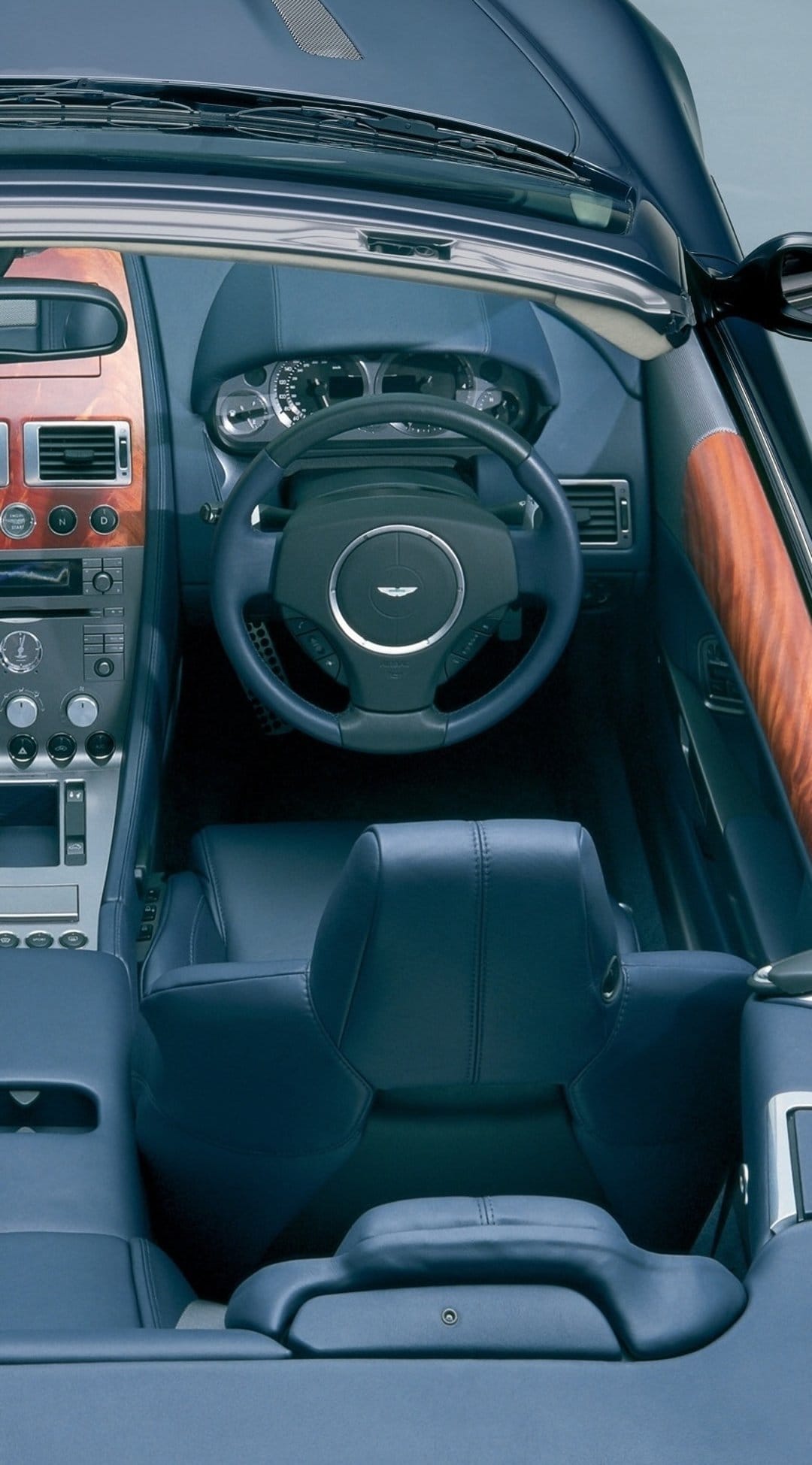 Navy blue leather seats and a polished wood dashboard inside an Aston Martin car cabin with a steering wheel.