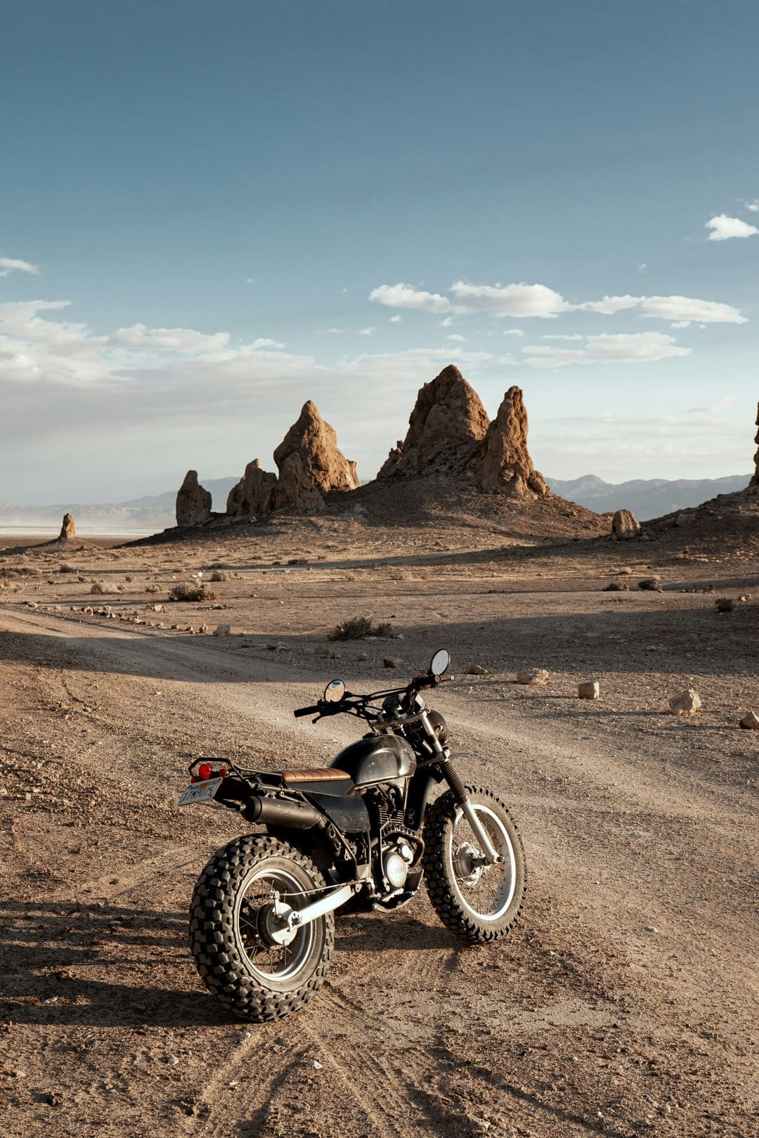Adventure motorcycle parked on a dirt road beside towering desert rock formations under a bright blue sky.