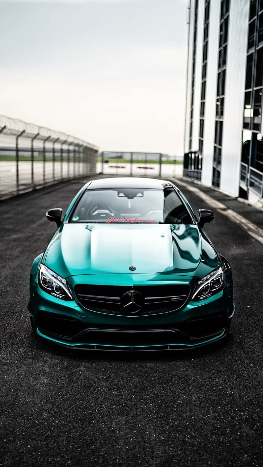 Emerald green Mercedes-AMG C63 parked on a dark asphalt racing track with sharp headlights and a metallic finish.