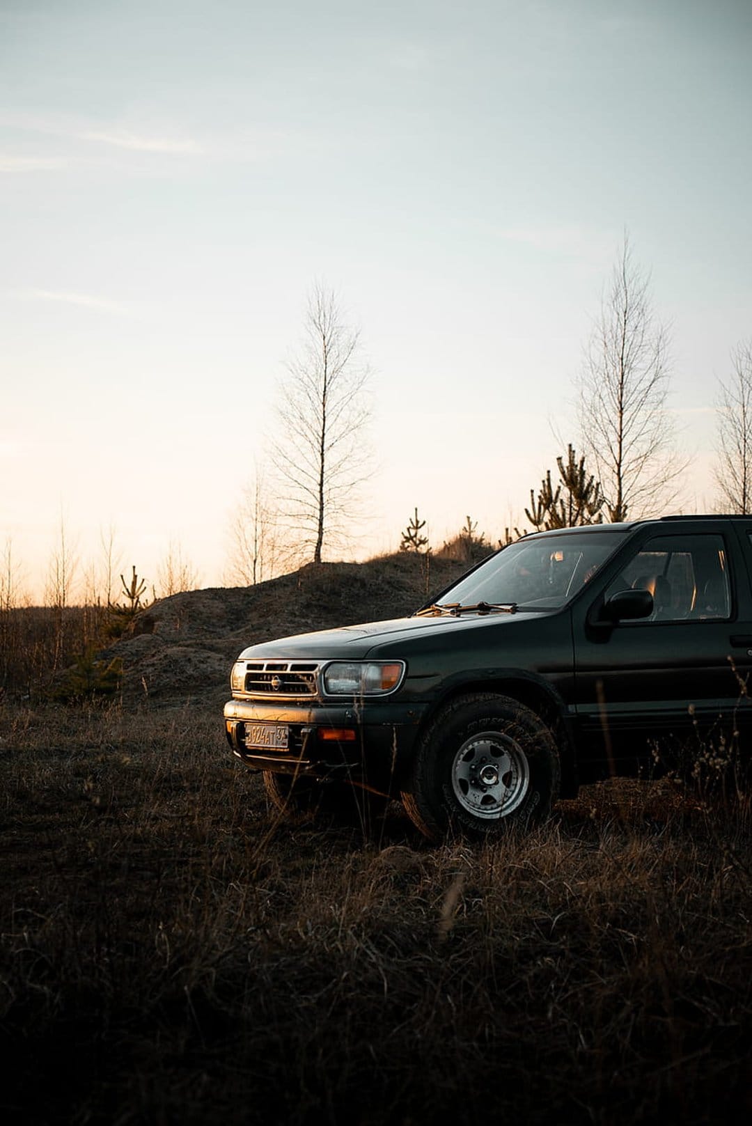 Dark SUV with rugged tires parked in a field of dry yellow grass during a warm orange and blue sunset.