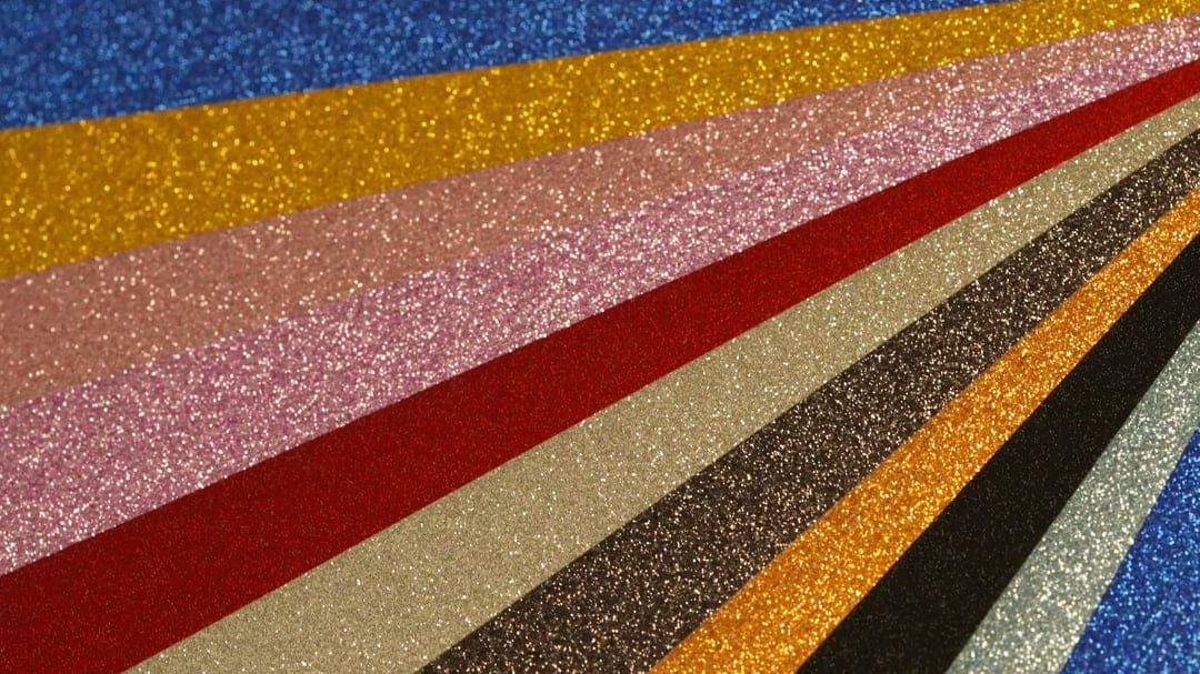Vertical strips of textured glitter paper in blue, red, gold, and pink colors with a sparkling finish.