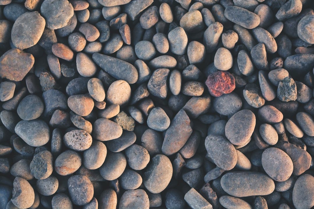 Smooth gray river rocks and one vibrant red stone captured in a close-up overhead shot for a textured phone backdrop.