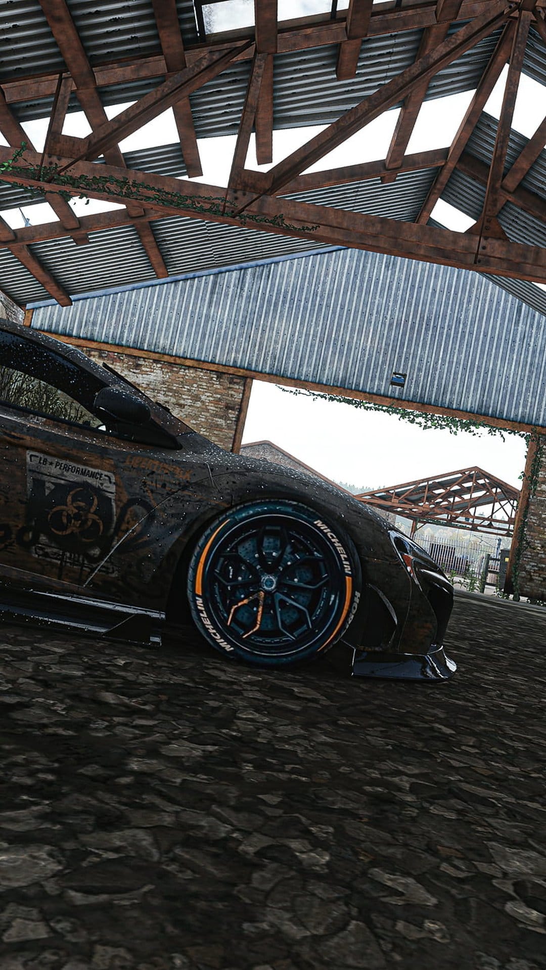 Rusted vintage car with orange rims parked under a decaying barn roof with green vines and corrugated metal.