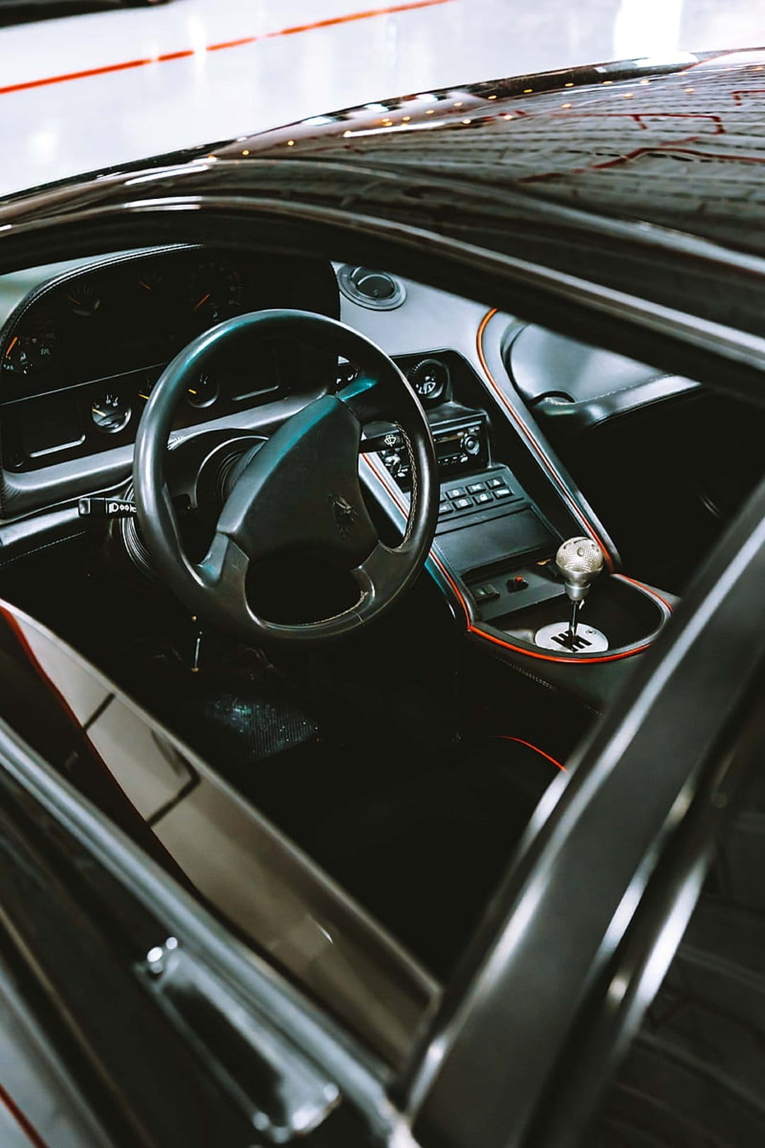 Black leather steering wheel and a metallic gear shifter with red trim inside a high-end sport car cockpit.