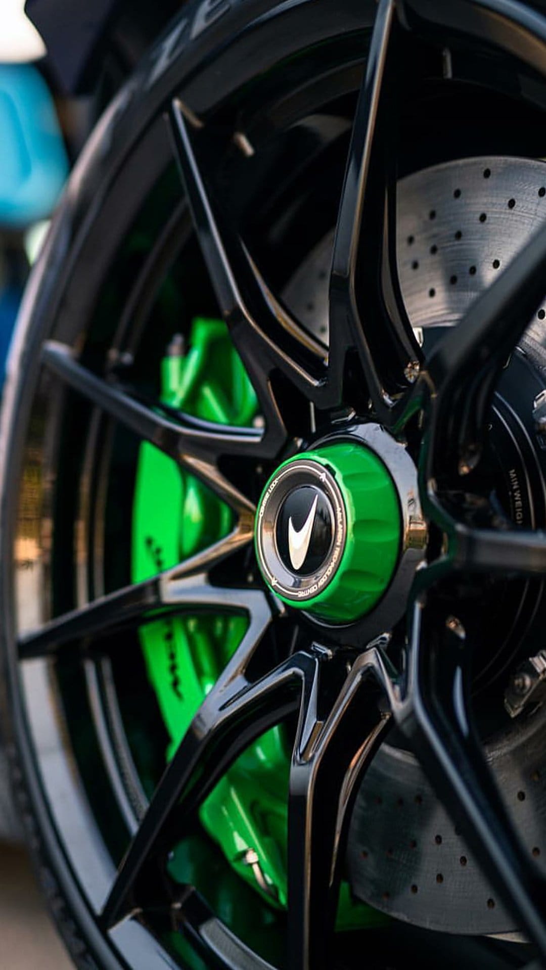 McLaren black alloy wheel featuring a vibrant green brake caliper and perforated disc on a vertical car wallpaper.