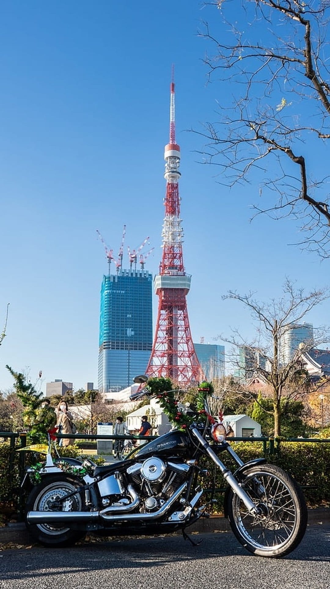 Harley Davidson cruiser parked on asphalt near Tokyo Tower under a clear blue sky with festive green decorations.