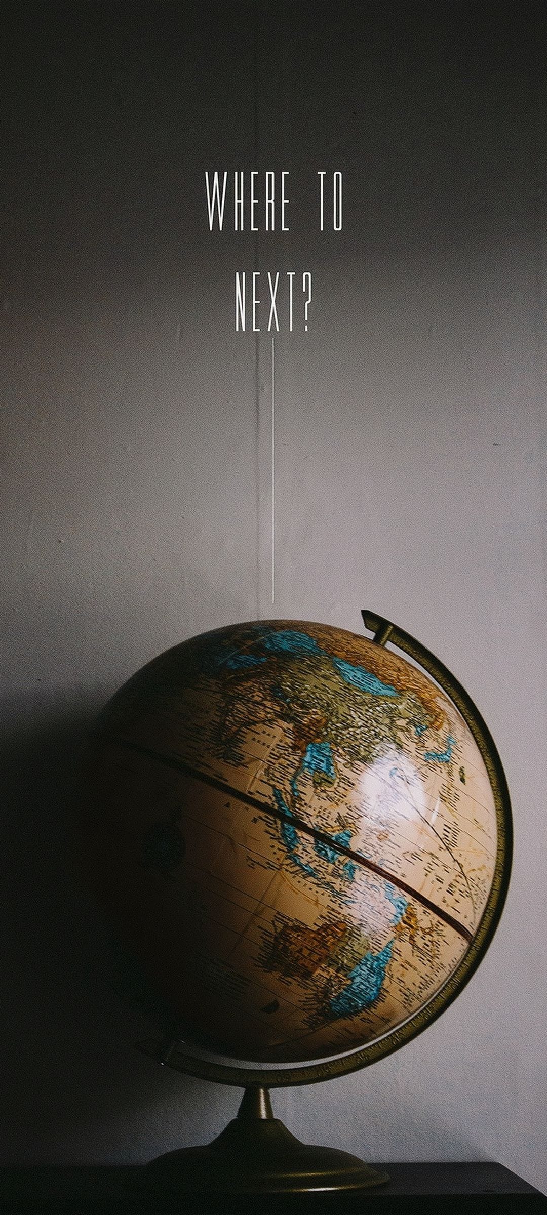 Vintage globe with aged maps rests below the white serif text reading WHERE TO NEXT on a soft-focus background.