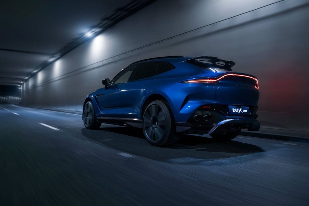 Rear view of a blue Aston Martin DBX 707 driving fast through a modern tunnel with motion blur and red tail lights.