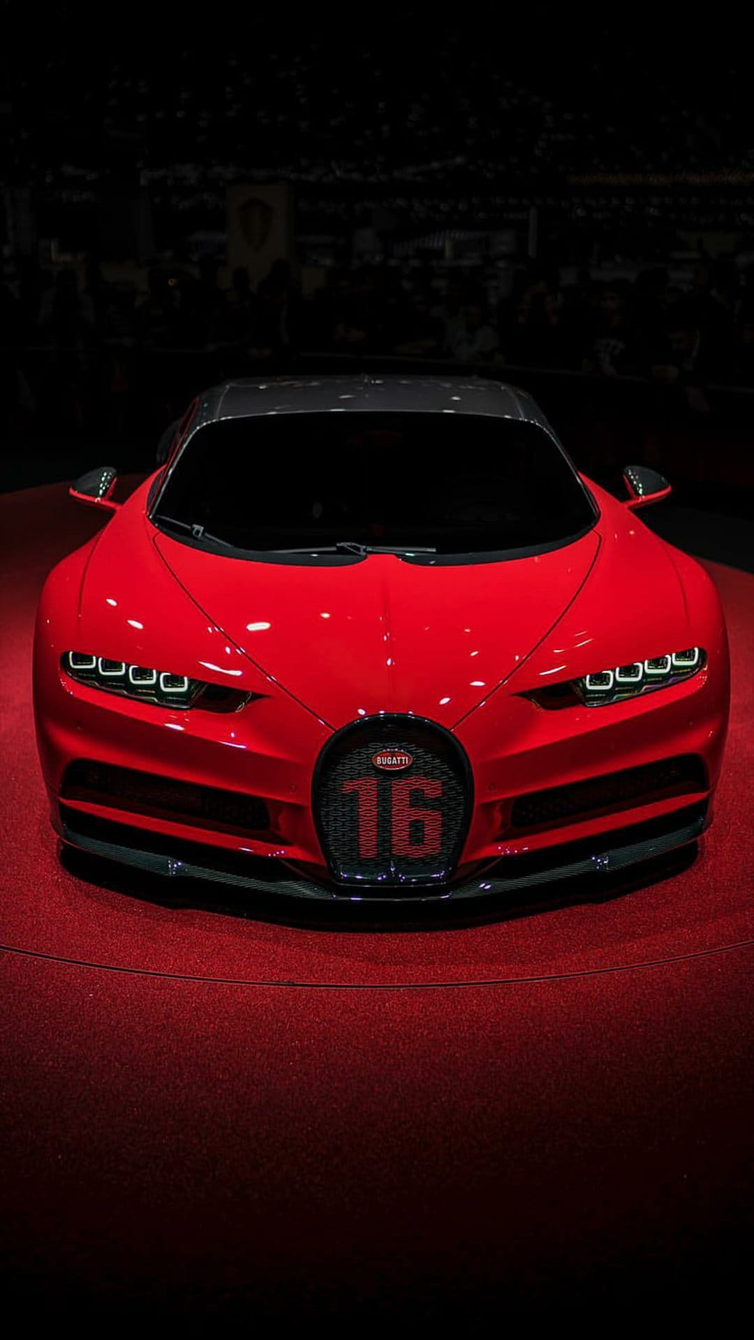 Red Bugatti Chiron hypercar on a red carpet with glowing headlights and 16 emblem on the horseshoe grille.