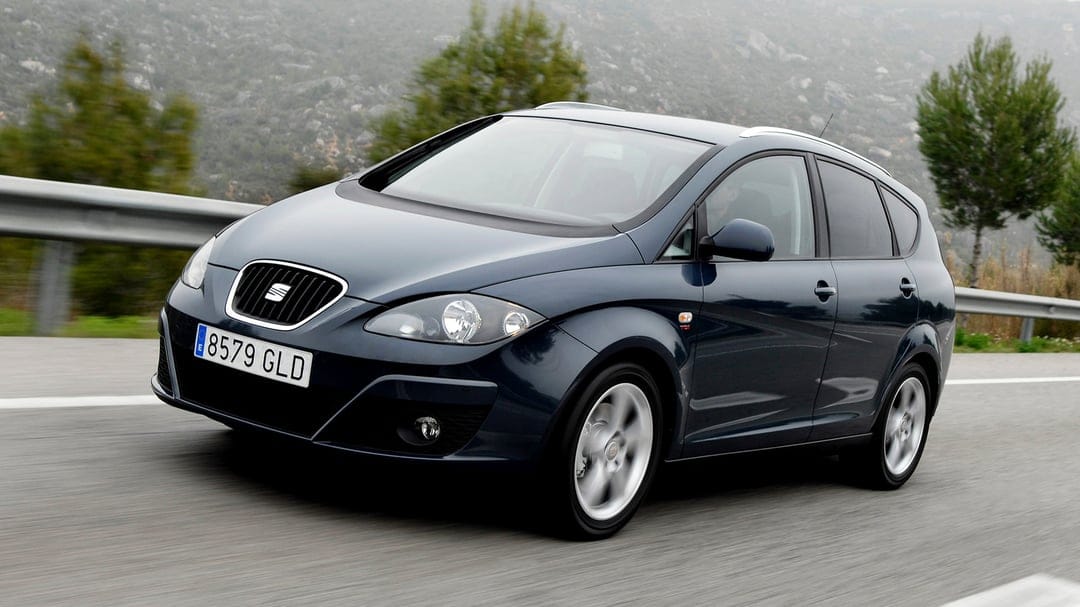 Dark blue SEAT Altea XL driving on a road with blurred mountain scenery and green trees in the background.