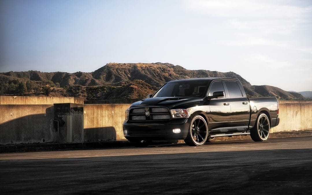 Black custom Dodge Ram truck with large rims parked on a concrete ledge overlooking brown hills at sunset.