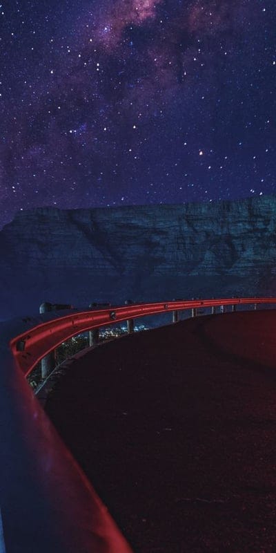 Night sky, Milky Way, road, stars, red, guardrail, cosmic, landscape, astronomy, long exposure, celestial, nature, travel, journey, dramatic, vibrant, dark, stunning, scenic, outdoors.
