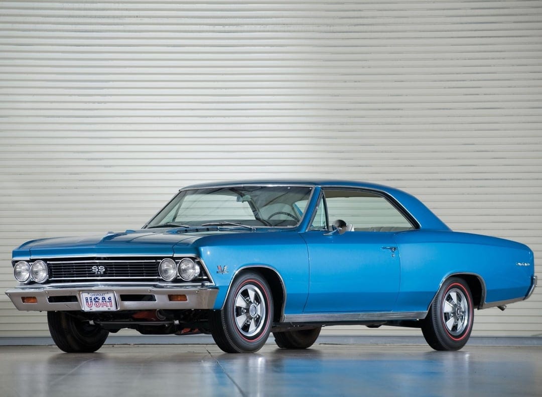 Blue 1966 Chevrolet Chevelle SS 396 classic muscle car with chrome accents parked against a white garage door.