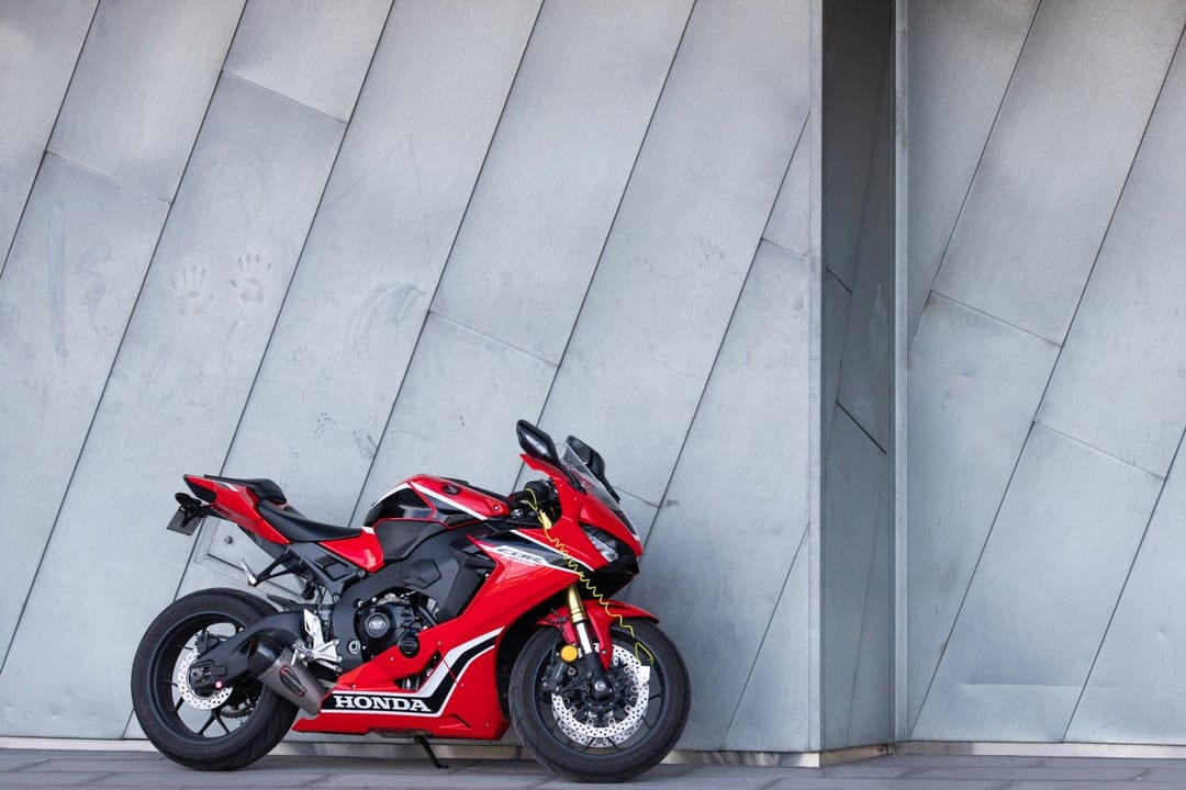 Red Honda motorcycle with black accents parked in front of a modern grey metal building with overlapping panels.