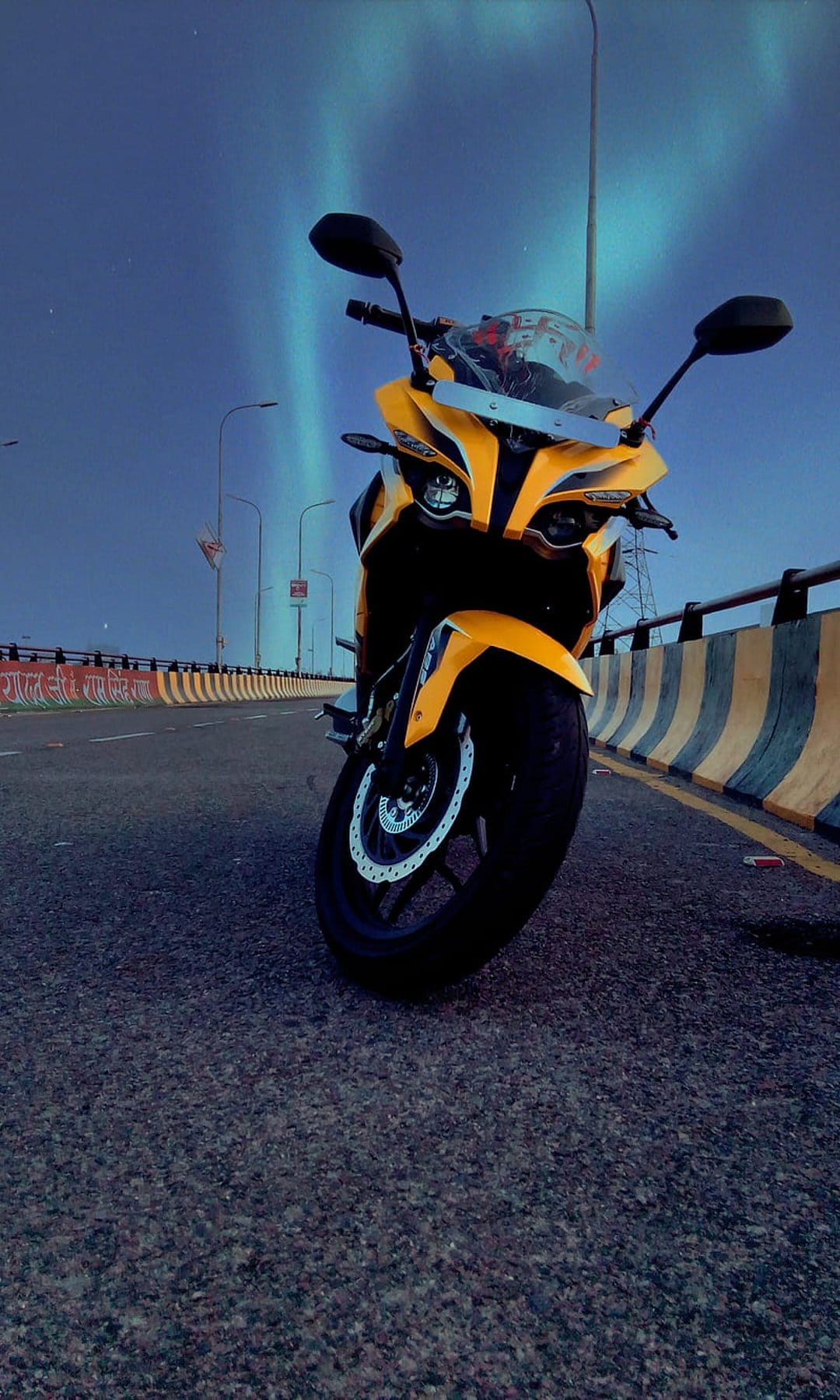 Yellow sport motorcycle on asphalt under green aurora borealis ribbons and glowing streetlights at night.