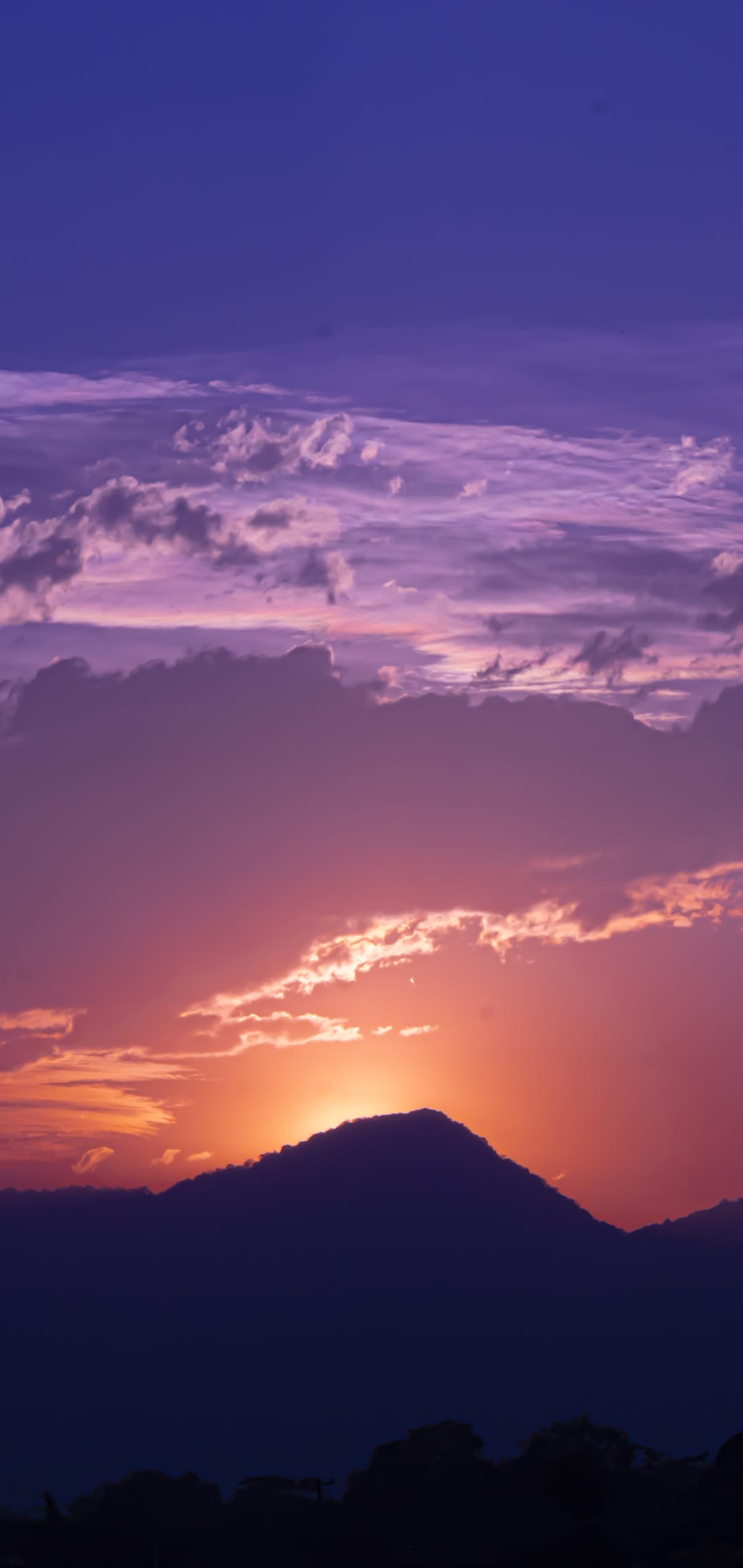 Jagged mountain peak silhouetted against a vibrant purple and orange twilight sky with scattered soft cloud wisps.