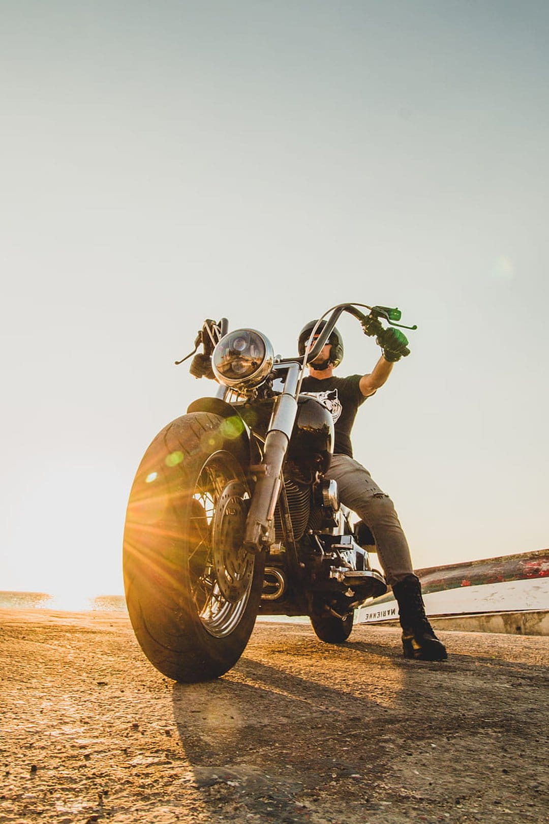 Motorcyclist in a helmet sits on a black cruiser motorcycle against a bright sunset with a warm lens flare.