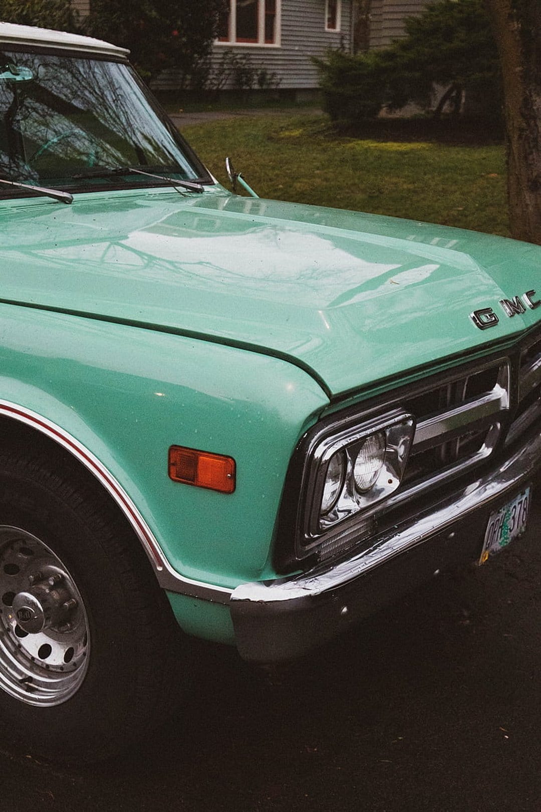 Vintage turquoise GMC pickup truck hood and chrome grille reflecting a soft overcast sky on a damp day.