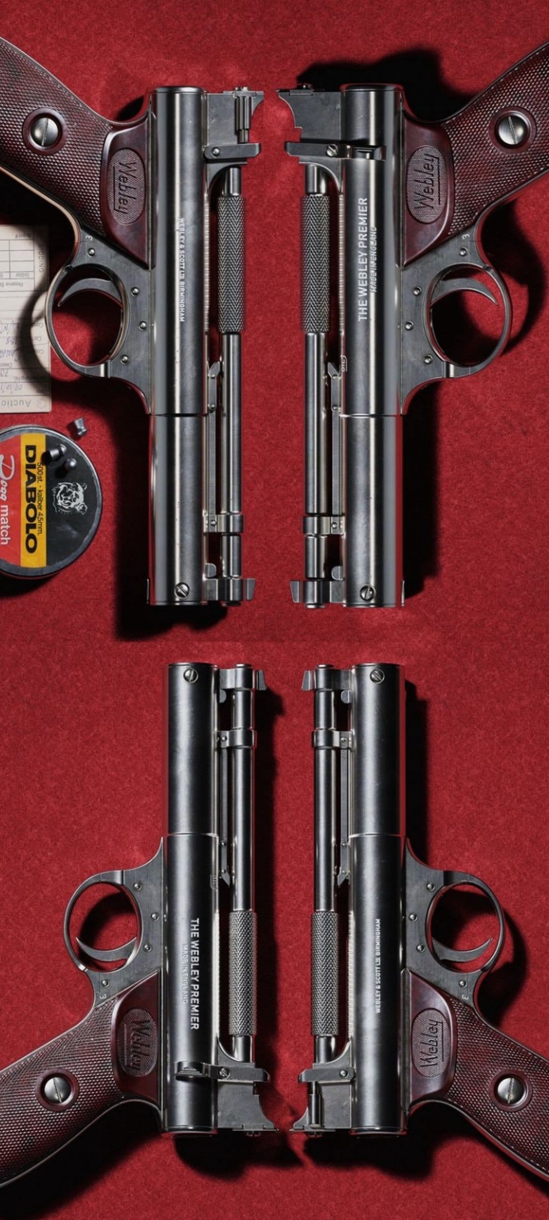 Two Webley Premier air pistols symmetrically arranged on red felt with a pellet tin and loose metal pellets.