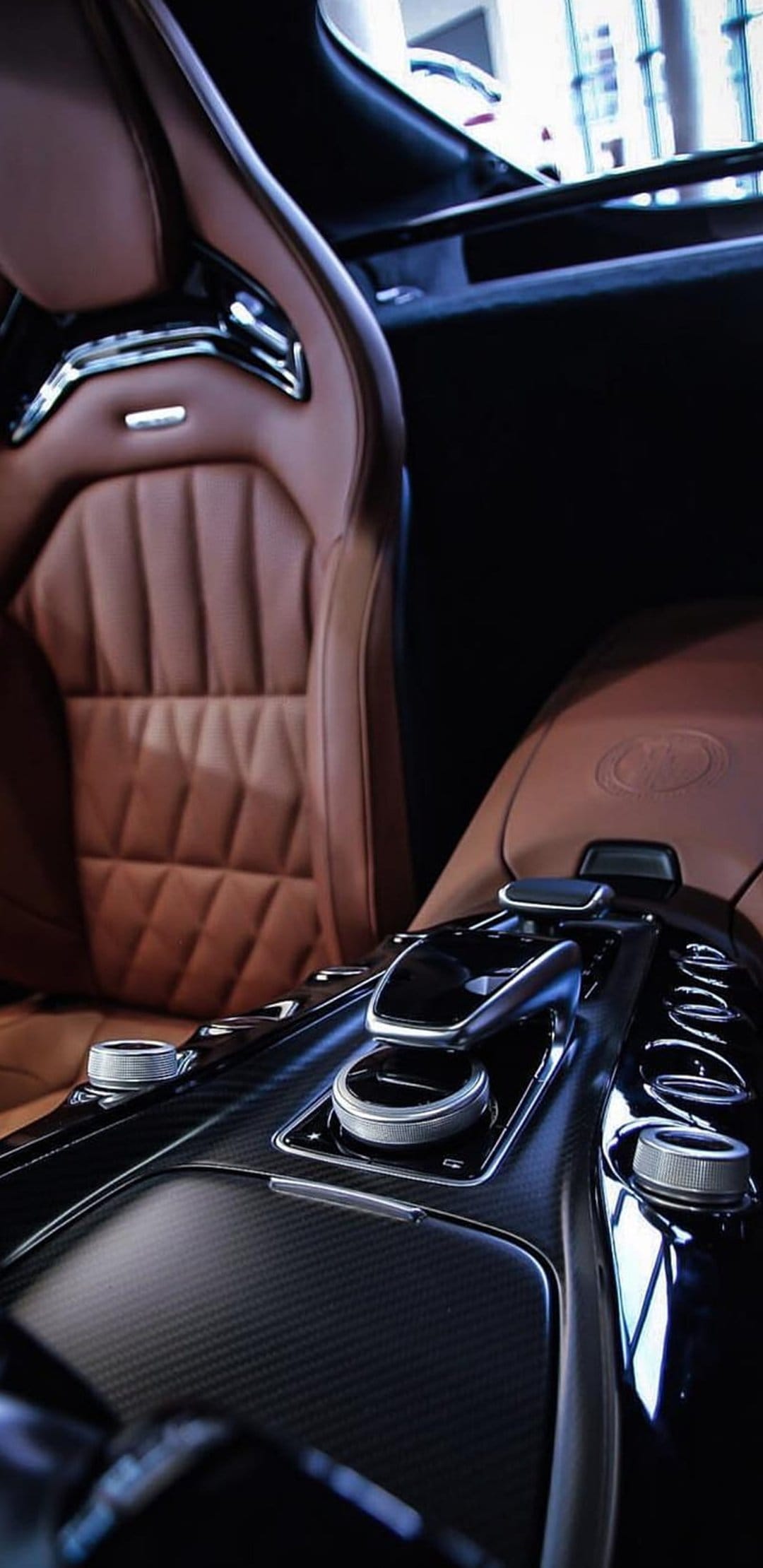Brown leather seats with diamond stitching next to a carbon fiber gear console and metallic control dials.