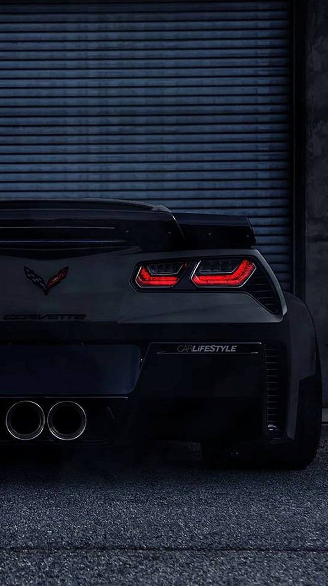 Chevrolet Corvette Z06 rear emblem and LED tail lights centered against a ribbed blue metal industrial garage door.