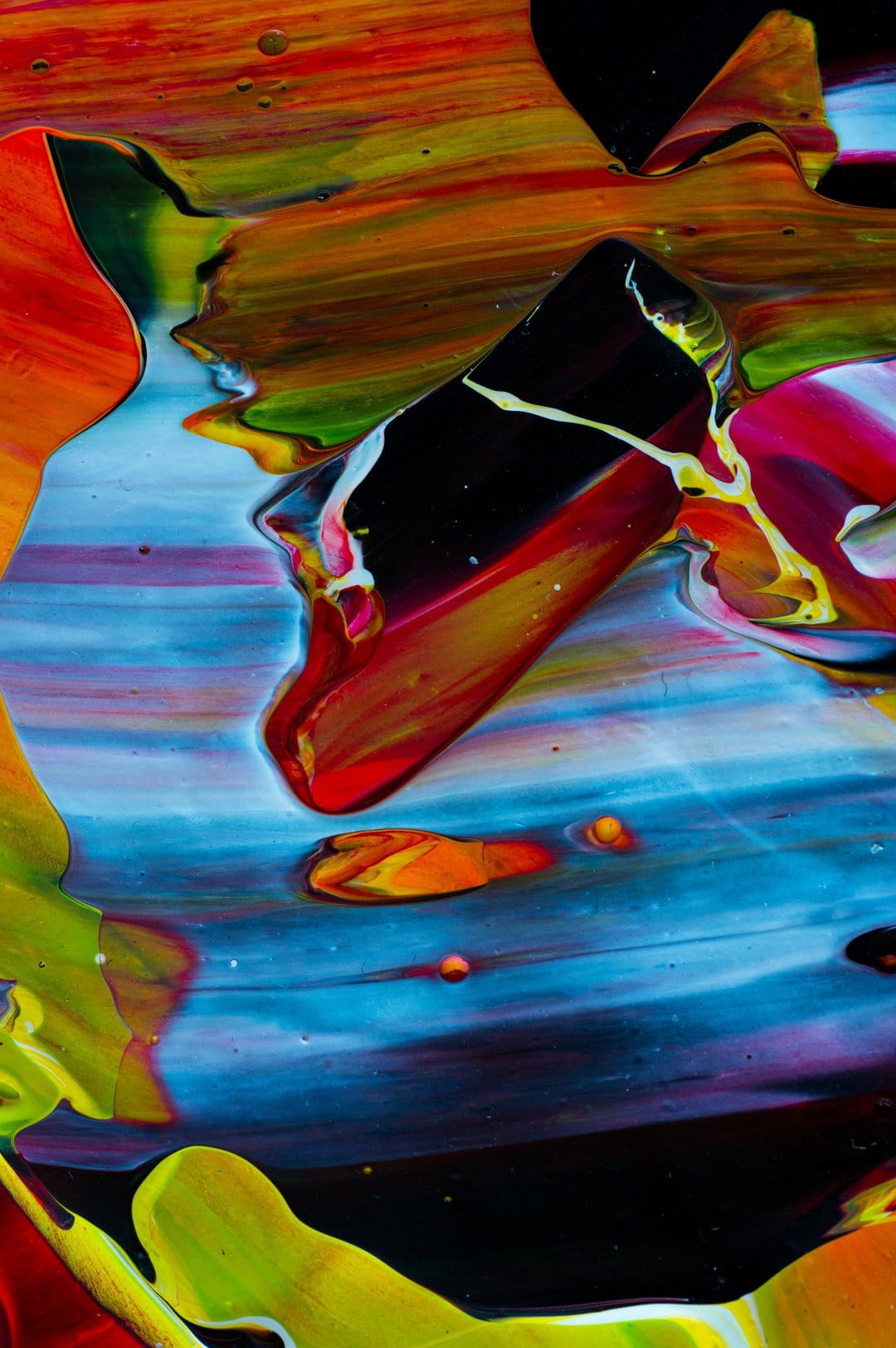 Red, blue, and yellow oil paints swirl into fluid marble textures with microscopic details and dark shadows.